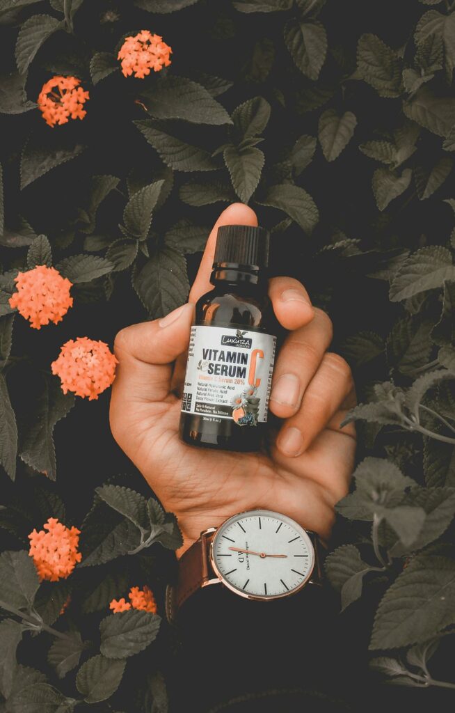 Brightly colored bottle of Vitamin C serum surrounded by fresh oranges and greenery, showcasing its natural ingredients and benefits for glowing skin.